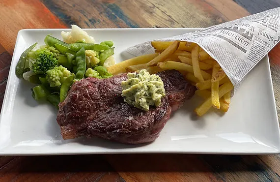 Faux-filet de bœuf à la plancha avec beurre Café de Paris, frites et petits légumes.