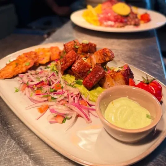 Chicharron con patacones, pancetta croustillante sur un lit de banane plantain frite, guacamole et salade d’oignons rouges à la coriandre
